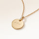 Close-up of a round gold pendant with a zirconia-set bail and personalised engraving of initials with a heart
