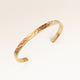 Close-up of minimalist bangle bracelet in gold with rippled wave surface and space for personalized engraving