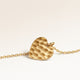 Close-up of minimalist heart-shaped heart pendant in gold with rippled wave surface and space for engraving on back