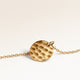 Close-up of minimalist round pendant in gold with rippled wave surface and space for engraving on back