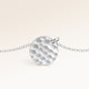 Close-up of minimalist round pendant in silver with rippled wave surface and space for engraving on back