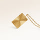 Close-up of minimalist square pendant in gold with ribbed sunburst surface and space for engraving on back