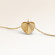 Close-up of minimalist heart pendant in gold with ribbed sunburst surface and space for engraving on the back.