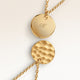 Close-up of two round pendants in gold – rippled front and polished back with an engraved initial
