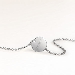 Back of a round silver necklace with a personal engraved date
