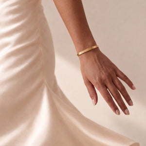 Model in cremefarbenem Satinkleid mit personalisiertem Bangle-Armreif in Gold mit eingraviertem Datum