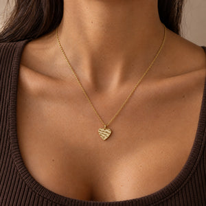 Model wearing a heart-shaped gold necklace with a rippled wave surface and space for personal engraving of text, coordinates or handwriting on the back