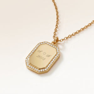 Close-up of an octagon gold pendant with white zirconia around the edge and a personal engraving of initials with a heart and a year