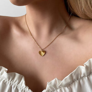 Personalized heart-shaped gold necklace with ribbed sunburst pattern and space for engraving of text or coordinates on the back