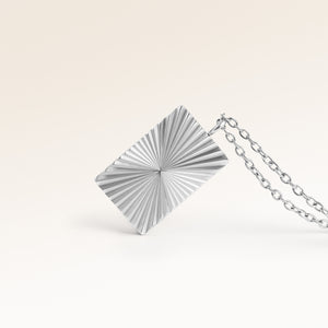 Close-up of minimalist square pendant in silver with ribbed sunburst surface and space for engraving on back