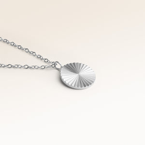Close-up of minimalist round pendant in silver with ribbed sunburst surface and space for engraving on back
