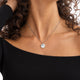 Model in a black top wearing a round silver necklace with a ridged sunburst pattern and room for personal engraving of text, coordinates or handwriting on the back