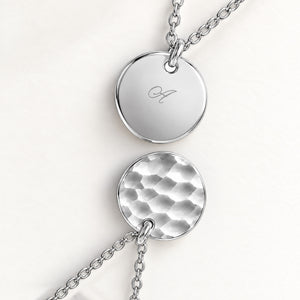 Close-up of two round pendants in silver – rippled front and polished back with an engraved initial